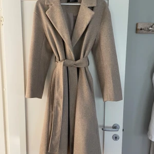 Beige kappa - Jag säljer nu en jättefin beige kappa som är som ny då den kommit till användning, max två gånger! Den är i ett fint skick och inga defekter förekommer. Fint skuren och med slits på baksidan samt fickor vilket jag tycker är snyggt!