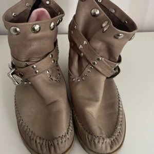 L di R Beige boots med nitar och broderad detalj - Säljer ett par unika beige boots i skinn med coola nitar och broderade detaljer på hälen. De har en avslappnad passform och är perfekta för höst och vår. Skorna har en dekorativ rem med spänne och är i välanvänt skick.