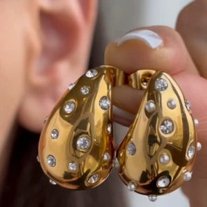 Guldörhängen med glittriga stenar - Eleganta guldörhängen med en unik droppform och glittriga stenar.De är i nyskick.Använt endast en gång.Vet ej vilket material det är, men köpt på Uropenn. Postas inom tre dagar efter köp.