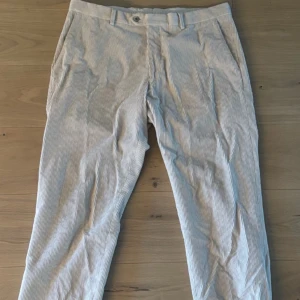  Oscar Jacobson byxor - Säljer ett par stiliga randiga byxor från Oscar Jacobson. De är i en ljus färg med diskreta ränder och har en klassisk passform. Perfekta för både vardag och festliga tillfällen. Byxorna är i oavänt skick. Skriv för mer bilder!