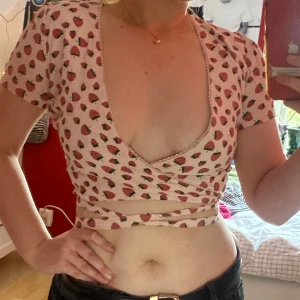 Rosa croptop - En supersöt rosa croptop med jordgubbstryck från Sugarthrillz! Långa snören som man kan knyta hur man vill och använd 2 gånger. 