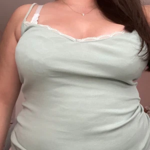 Mintgrön linnetopp med spetsdetaljer - Säljer en söt mintgrön linnetopp med smala axelband och spetsdetaljer vid halsringningen. Perfekt för sommardagar eller som ett lager under en kofta. Toppen är i ett mjukt och bekvämt material.