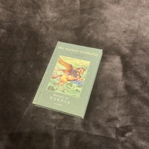 Min morbror trollkarlen - Säljer boken 'Min morbror trollkarlen' av C.S. Lewis. Det är en del av serien 'Berättelsen om Narnia'. Boken har ett grönt omslag med en illustration av en bevingad häst. Perfekt för fantasyälskare och samlare av Narnia-serien!