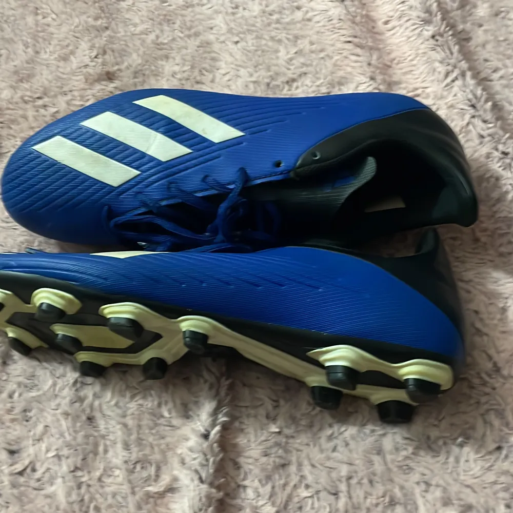 Säljer ett par snygga blå fotbollsskor från Adidas med vita detaljer. Skorna har snörning och är i nyskick. Perfekta för fotbollsträning eller match. De har en klassisk design med tre vita ränder på sidan och svarta detaljer vid hälen. Pris kan diskuteras 🙌. Skor.