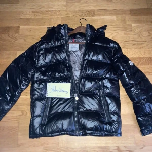 Moncler Maya - Säljer en snygg och varm svart dunjacka från Moncler. Jackan har en glansig finish och är perfekt för kalla vinterdagar. Kvitto finns.