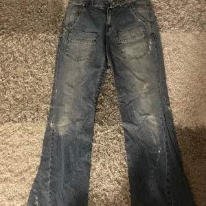True religion jeans - Säljer ett par blå jeans från True Religion med coola slitningar och en vintage look. Mått: midja 40cm längd 115cm bredd 27cm benöppning 27cm