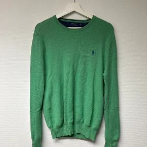 Grön tröja från Ralph Lauren - Säljer en snygg grön tröja från Ralph Lauren i storlek M. Den har en klassisk design med rund hals och det ikoniska blå logotypbroderiet på bröstet. Perfekt för både vardag och lite finare tillfällen. Tröjan är i nyskick och redo för en ny ägare! Bara använd vid 1 tillfälle. 