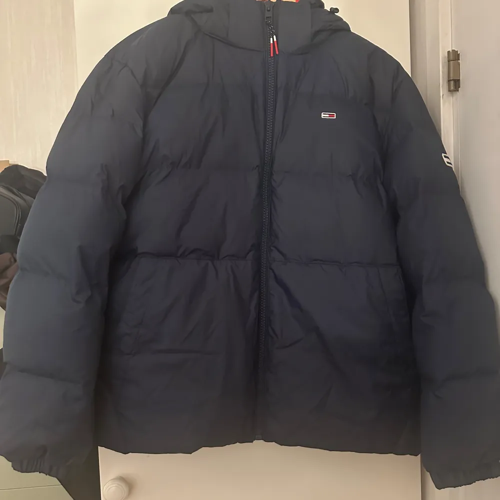 Blå puffer jacka från Tommy Hilfiger i storlek M. Helt ny/oanvänd med prislapp kvar och säljs på grund av att den aldrig kommit till användning. Fin passform och passar bra framåt kallare årstider. Luvan är avtagbar!. Jackor.