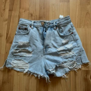 Ljusa jeansshorts från Pull&Bear - Säljer ett par ljusa jeansshorts från Pull&Bear i storlek EUR 32. De har en cool distressed look med slitningar fram och fransiga kanter. Perfekta för sommaren och ger en avslappnad stil. Passar bra till både vardag och fest!