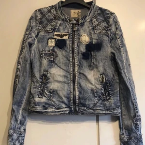 Jeansjacka med patches från The Culture - Säljer en cool jeansjacka från The Culture i storlek S. Den har en snygg sliten look med flera patches och nitar på kragen. Jackan har dragkedja och långa ärmar med stjärndetaljer. Perfekt för en avslappnad stil!
