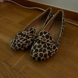 Leopardmönstrade ballerinaskor med guldkedja - Snygga ballerinaskor i leopardmönster. De har en dekorativ guldkedja framtill som ger en extra touch. Perfekta för både vardag och fest!