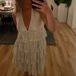 Glittrig vit klänning - Säljer en superfin glittrig vit klänning med volanger. Den är perfekt för fest och har en djup v-ringning. Klänningen är ärmlös och har en kort längd som ger en härlig sommarkänsla. Perfekt för att glänsa på nästa party! ✨