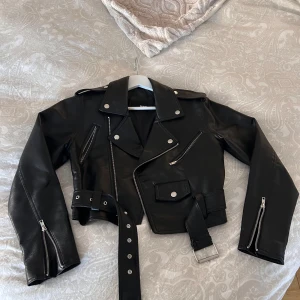 Svart skinnjacka - Säljer en snygg svart skinnjacka i klassisk bikerstil. Jackan har coola dragkedjor och ett bälte i midjan för extra edge. Perfekt för höst och vår, och funkar lika bra till fest som till vardags. Den är i mycket bra skick och redo för nya äventyr! 🖤