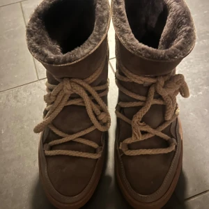Bruna vinterboots från Inuikii - Säljer ett par mysiga och varma bruna vinterboots från Inuikii. De har en fluffig insida och rejäla snören för en säker passform. Perfekta för kalla vinterdagar! 🥶På blid 3 kan man se att ena snöret lossnat från sidan men det går enkelt att fixa!