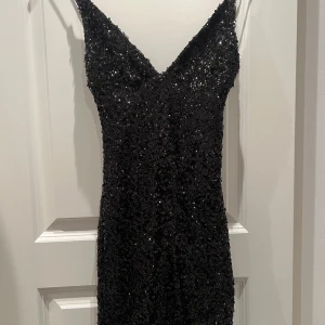 Svart glittrig fest klänning - Snygg svart klänning från Rebecca Stella i storlek XS. Den är glittrig och perfekt för festliga tillfällen. Klänningen har en tight passform och smala axelband, vilket ger en elegant look. Perfekt för nyår eller andra speciella tillfällen! Jag säljer då jag köpte för liten storlek men tycker den är JÄTTESNYGG!