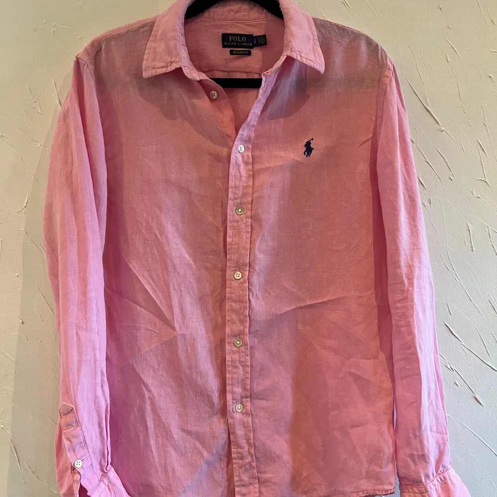 Säljer en snygg rosa skjorta från Ralph Lauren i storlek S. Skjortan är i bomull och har en klassisk krage med knappar hela vägen ner. Den har långa ärmar och en broderad logga på bröstet. Perfekt för både vardag och fest!. Skjortor.