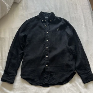 Svart skjorta från Polo Ralph Lauren - Säljer en stilren svart linneskjorta från Polo Ralph Lauren i slim fit. Skjortan är långärmad och har klassiska knappar framtill. Perfekt för både vardag och fest! 🖤
