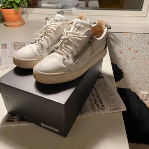 Vita sneakers från Giuseppe Zanotti - Säljer ett par vita sneakers från Giuseppe Zanotti i bra skick. Skorna har snörning och dragkedja på sidan. Storlek 43,5. De är självklart äkta. Billigare pris vid snabb affär!