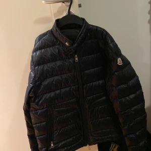 Svart pufferjacka från Moncler - Säljer en snygg svart pufferjacka från Moncler i mycket bra skick. Jackan har en quiltad design med dragkedja och Moncler-logga på ärmen. Perfekt för höst och vinter, håller dig varm och stilren. Passar både till vardags och festliga tillfällen!