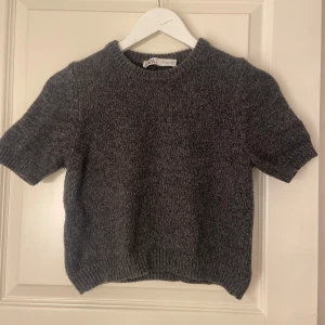 Grå stickad tröja från Zara - Säljer en superfin grå stickad tröja från Zara. Den är kortärmad och perfekt för både höst och vår. Tröjan har en ribbad kant vid ärmslut och nederkant, vilket ger en snygg passform. 🖤