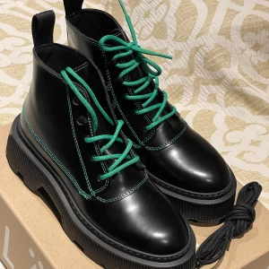 Svarta boots från LÄST - Snygga svarta boots i skinn från LÄST med gröna snören och detaljer. Perfekta för höst och vinter med sin robusta sula och stilrena design. De har en cool och modern look som passar både till vardags och fest. Helt nya och oanvända!