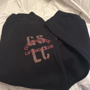 Svarta mjukisbyxor från Gymshark - Säljer ett par svarta mjukisbyxor från Gymshark i storlek XS. Perfekta för träning eller en chill dag hemma. Byxorna har elastisk midja och tryck med texten 'Gymshark Lifting Club' i rött och beige. Superbekväma och i bra skick!