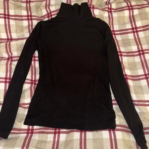 Svart ribbad polotröja från H&M - Säljer en stilren svart ribbad polotröja från H&M i storlek S. Perfekt för kyliga dagar med sin höga krage och långa ärmar. Tröjan är i bra skick och passar både till vardags och fest. Ett måste i garderoben! 🖤