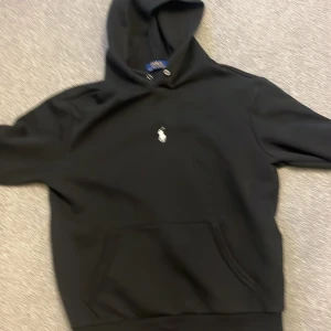 Svart hoodie från Polo Ralph Lauren - Säljer en klassisk svart hoodie från Polo Ralph Lauren i mycket bra skick. Den har en liten broderad logga på bröstet och en stor ficka framtill. Perfekt för både vardag och chill. 😎 