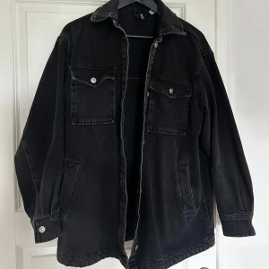 Svart jeansjacka - Säljer en svart jeansjacka i bra skick. Den har en klassisk design med två bröstfickor med knappar och två sidofickor. Jackan är långärmad och har en avslappnad passform, perfekt för höst och vår. Passar både till vardags och lite mer uppklädda tillfällen.