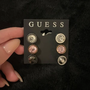 Örhängen från Guess i olika färger - Säljer ett set med tre par örhängen från Guess. De är runda med stenar i färgerna silver, rosa och svart. Står GUESS ingraverat på sidorna. Perfekta för att matcha olika outfits och tillfällen. Alla örhängen är i nytt skick, oanvända och kommer med originalförpackning. 💕