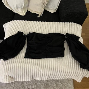 Svart offshoulder topp - Säljer en snygg svart offshoulder topp med långa puffiga ärmar. Toppen har en tight passform och är perfekt för festliga tillfällen. Materialet känns mjukt och bekvämt mot huden. Passar perfekt till både jeans och kjol för en chic look!