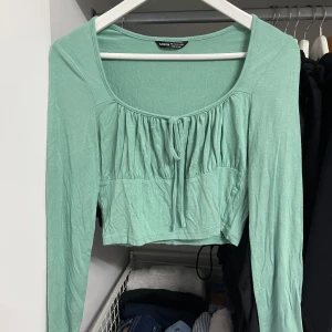 Grön långärmad topp från Shein - Säljer en söt grön långärmad topp från Shein i storlek S. Toppen har en knytning framtill och är croppad, vilket ger den en trendig look. Perfekt för vår och sommar!