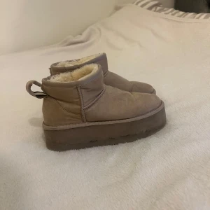 Höga Uggs - Beiga uggs med sula på 5cm från Nelly. storlek 37. använda under en vinter.  Tyvärr har jag en valp hemma som gärna tuggar på skor så ena flärpen har gått av, men enkelt att sy in alternativt klippa av båda två.  Köpta för 799kr och säker för 350kr