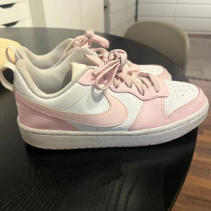 Nike sneakers i rosa och vit - Säljer ett par snygga Nike sneakers i rosa och vit. De har en klassisk design med snörning och en bekväm passform. Perfekta för vardagsbruk eller en avslappnad dag ute. Skorna är i bra skick och redo för en ny ägare!