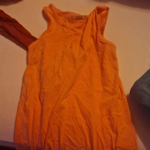 Orange ärmlös linnetopp - Säljer en snygg orange ärmlös linnetopp. Perfekt för sommardagar eller som ett lager under en jacka. Toppen är i ett mjukt och bekvämt material, vilket gör den idealisk för både vardag och fest. Passar bra till jeans eller shorts!