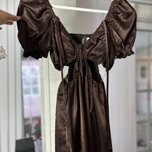 Brun klänning med puffärmar - Säljer en superfin brun klänning med puffärmar och knytning framtill. Den har en glansig finish som ger en lyx känsla.🤎