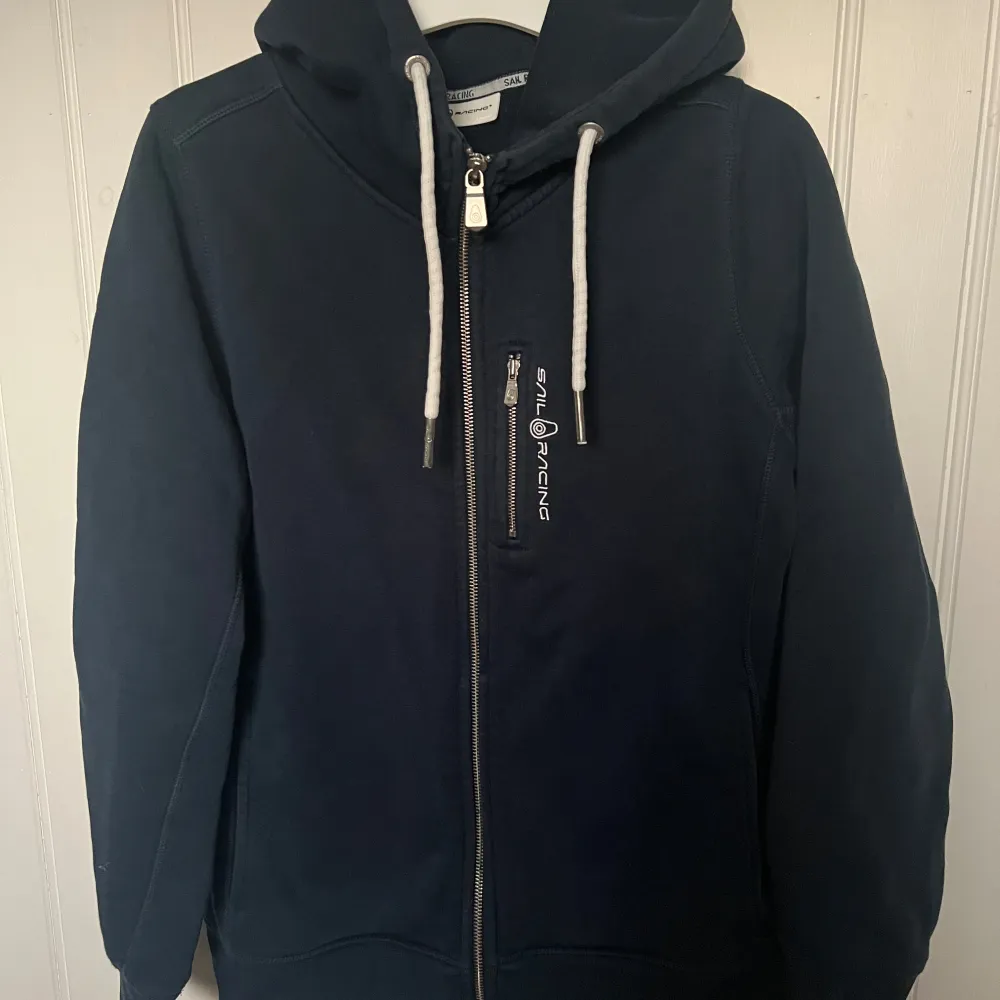 Sail Racing hoodie, nästintill oanvänd. Marinblå färg med text på ryggen.. Hupparit & Collegepaidat.