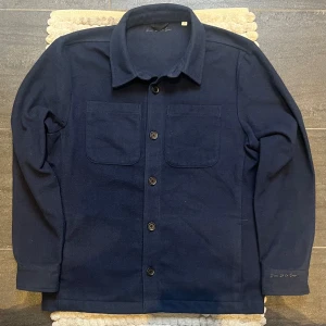 Donce De La Sense Overshirt Navy // Marinblå  - Säljer en snygg mörkblå overshirt från Donce De La Sense. Den har en klassisk krage och knappar framtill. Två praktiska bröstfickor och långa ärmar gör den perfekt för både vardag och fest. Materialet känns mjukt och skönt, perfekt för höst och vår.
