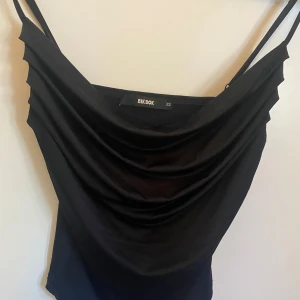 Svart linnetopp från Bik Bok - Säljer en stilren svart topp från Bik Bok i storlek XS. Toppen har tunna axelband och en draperad framsida som ger en snygg look. Perfekt för en utekväll eller fest! 🖤säljer pga att den endast använts en gång💗💗kan även passa S. Pris kan diskuteras 💗💗köpt för 199kr och använd 1 gång