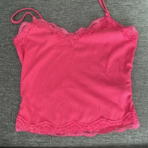 Rosa ribbad linnetopp med spetsdetaljer - Säljer en superfin rosa ribbad linnetopp med spetsdetaljer längs kanterna. Den har smala axelband och en söt spetskant både upptill och nedtill. Perfekt för sommardagar eller som ett lager under en kofta. Toppen är i bra skick och redo för nya äventyr! 💖