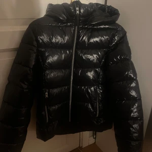 Svart pufferjacka från Everest - Snygg svart pufferjacka från Everest med glansig finish. Jackan har dragkedja framtill och två praktiska fickor med dragkedjor. Köpt för 699kr, jättefint skick och inte använd så många gånger.