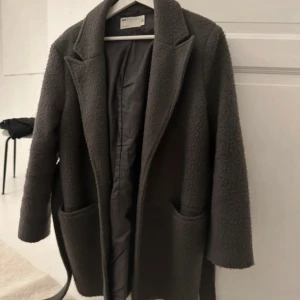 Grå kappa från ASOS DESIGN - Snygg grå kappa från ASOS DESIGN med bälte i midjan och stora fickor framtill. Perfekt för kyligare dagar med sin mysiga och stilrena design.