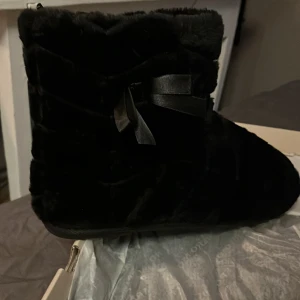 Svarta pälsboots med rosett - Snygga och mysiga svarta boots i pälsmaterial med en dekorativ rosett på sidan. Perfekta för att hålla fötterna varma under kalla dagar. Helt nya så edast provade. Säljer då som inte passade min smak