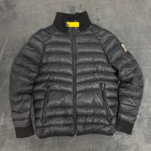 Svart pufferjacka från Parajumpers - Säljer en svart pufferjacka från Parajumpers med dragkedja och ribbad krage. Jackan har en broderad detalj på ärmen och är perfekt för kyligare väder. Den är långärmad och har en stilren design. En skada på baksidan av högra armen och en till småskada på bröstet. Hör av dig 