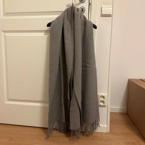 Grå halsduk med fransar - Snygg och stilren grå halsduk med fransar i ändarna. Perfekt för att hålla dig varm under kyliga dagar. Den neutrala färgen gör den lätt att matcha med olika outfits.