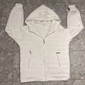 Vit Cardigan - Säljer en stilren vit cardigan med dragkedja framtill. Jackan har en praktisk huva och två fickor med dragkedjor. Perfekt för en avslappnad look. Testad 1 gång annars helt oanvänd och jag säljer den pga att den inte kommer till användning.🙃Cardiganen är från Lingsen. Tveka inte att kontakta vid fler frågor.