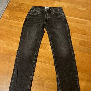 Svarta jeans från Lindex - Snygga svarta jeans från Lindex i en klassisk straight fit. Perfekta för en stilren look med fem fickor och knappgylf. Passar både till vardags och mer uppklädda tillfällen.