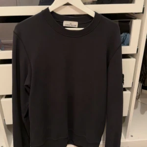 Svart tröja från Stone Island - Säljer en stilren svart tröja från Stone Island med deras ikoniska märke på ärmen. Tröjan har en klassisk rund hals och långa ärmar, perfekt för en avslappnad look.