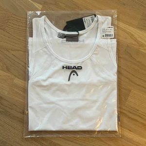 Vit linnetopp från Head - Dam - Säljer en vit linnetopp från Head, perfekt för träning. Toppen är ärmlös med rund halsringning och har en stilren design med Head-loggan på bröstet. Materialet är lätt och andas bra, vilket gör den idealisk för aktiva dagar. Helt ny, nypris ca 400kr