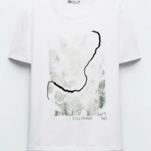 Vit t-shirt med abstrakt tryck - vit t-shirt med ett abstrakt svart och grått tryck på framsidan. Texten 'STILL FRAME 34/1' finns under trycket. 